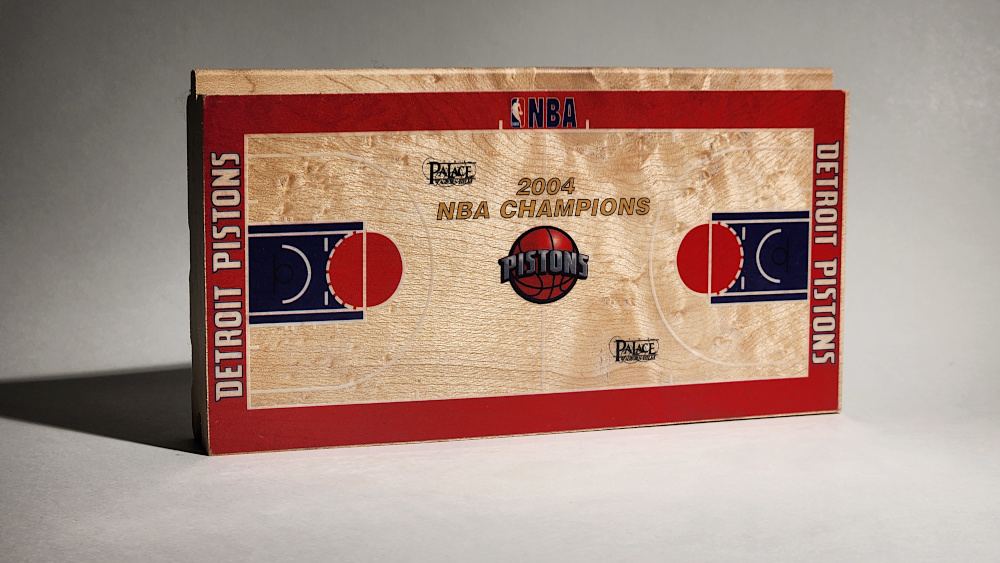 A replica of the Detroit Pistons 2004 NBA Champions basketball floor shown on a piece of hardwood flooring by Horner Sports Flooring