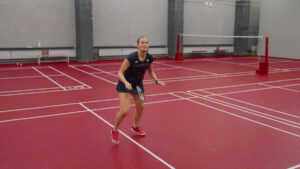 a woman playing badminton on red polyurethane gym flooring.